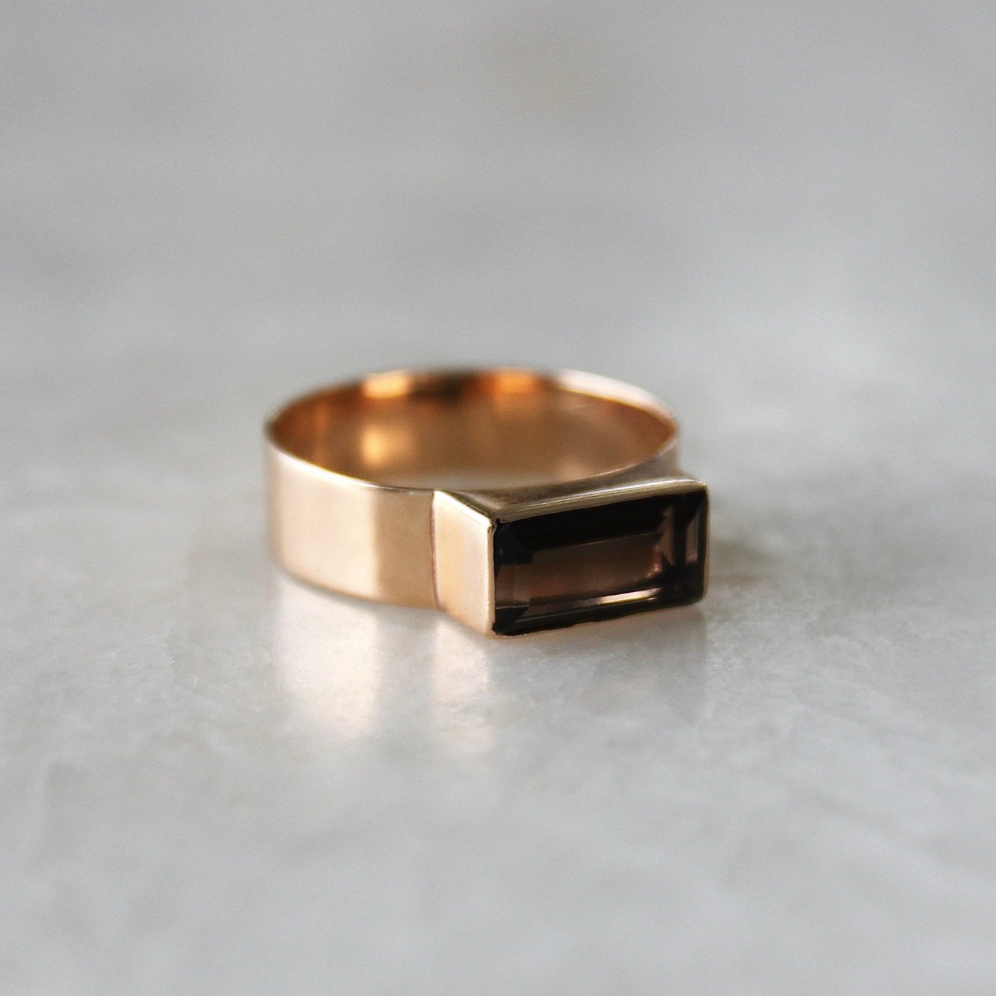 Gold ring with a rectangular gemstone on a light gray background