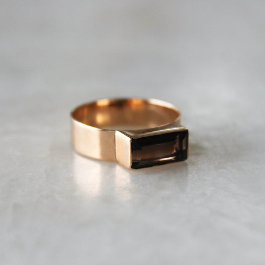 Gold ring with a rectangular gemstone on a light gray background